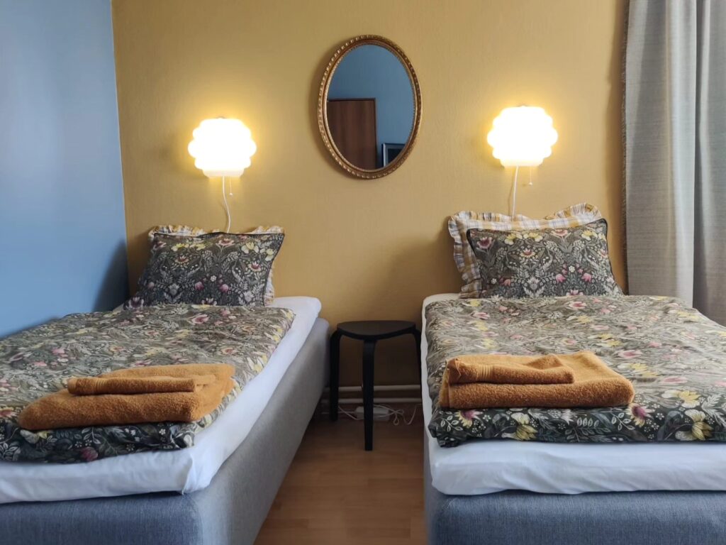Kuvassa on kaksi sänkyä ja seinälamppua hotellihuoneessa.