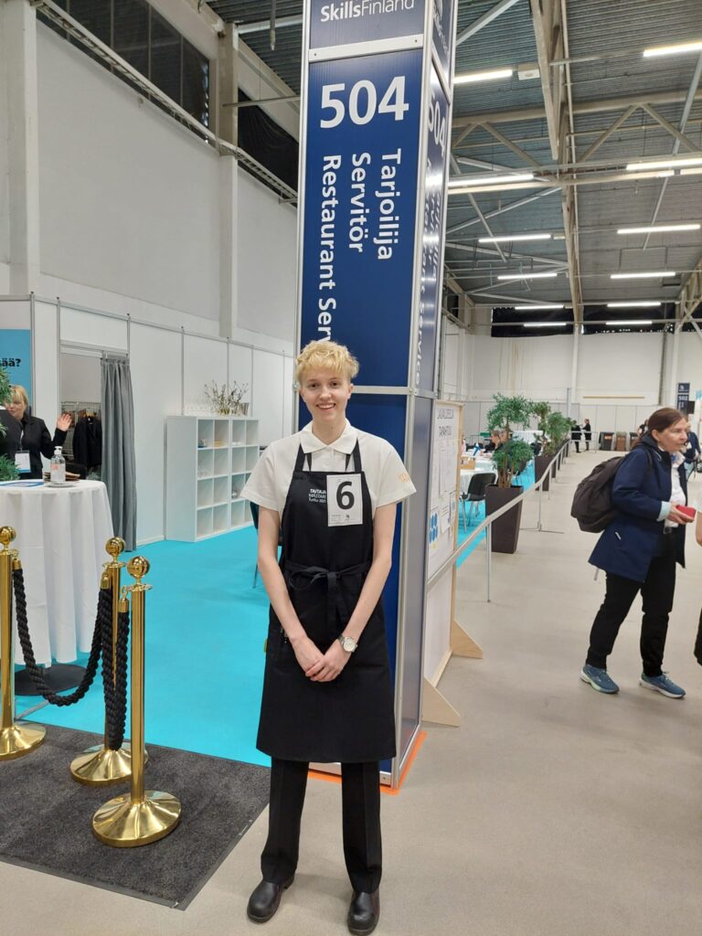 Taitaja-finalistimme kuva tarjoilija-lajin pylvään edessä.