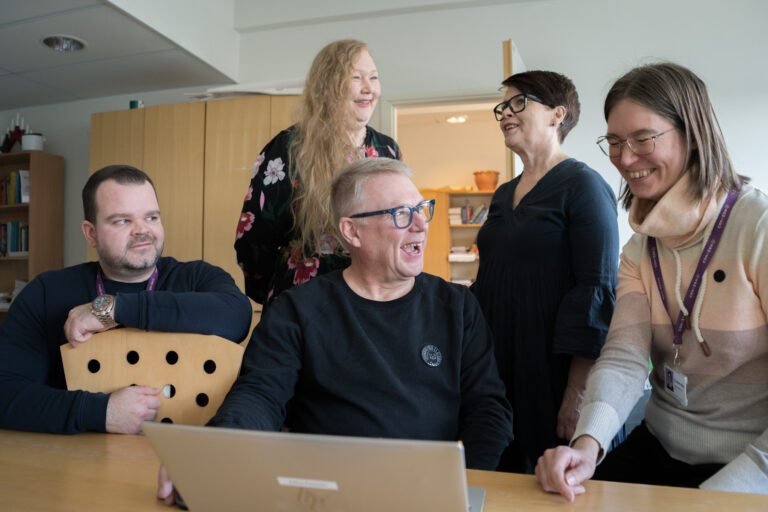 Kuvassa on viisi opetushenkilöstömme jäsentä, jotka keskustelevat iloisesti.