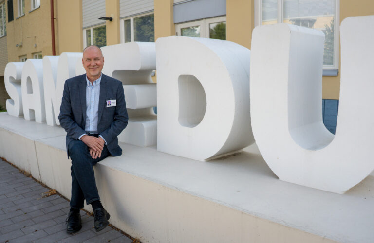 Kuntoyhtymän johtaja, rehtori istuu Samiedu-kyltin edessä.