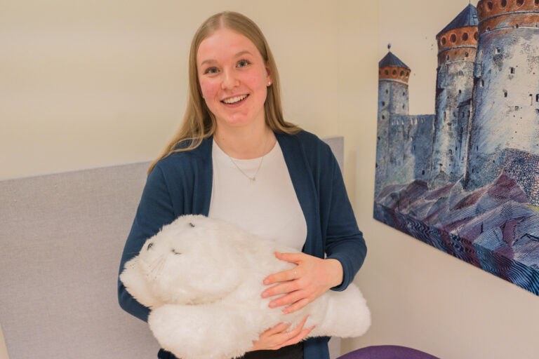 Kuvassa on jutun nuori nainen sylissään hoitoavusteena käytettävä pehmonorppa.