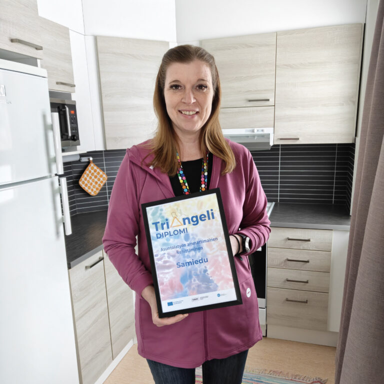 Mervi pitää käsissään diplomia. Kuva on otettu asuntolan soluasunnon keittiössä.