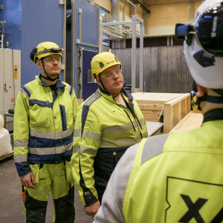 Kaksi opiskelijaa seuraavat työnohjaajan puhetta rakennustyömaalla