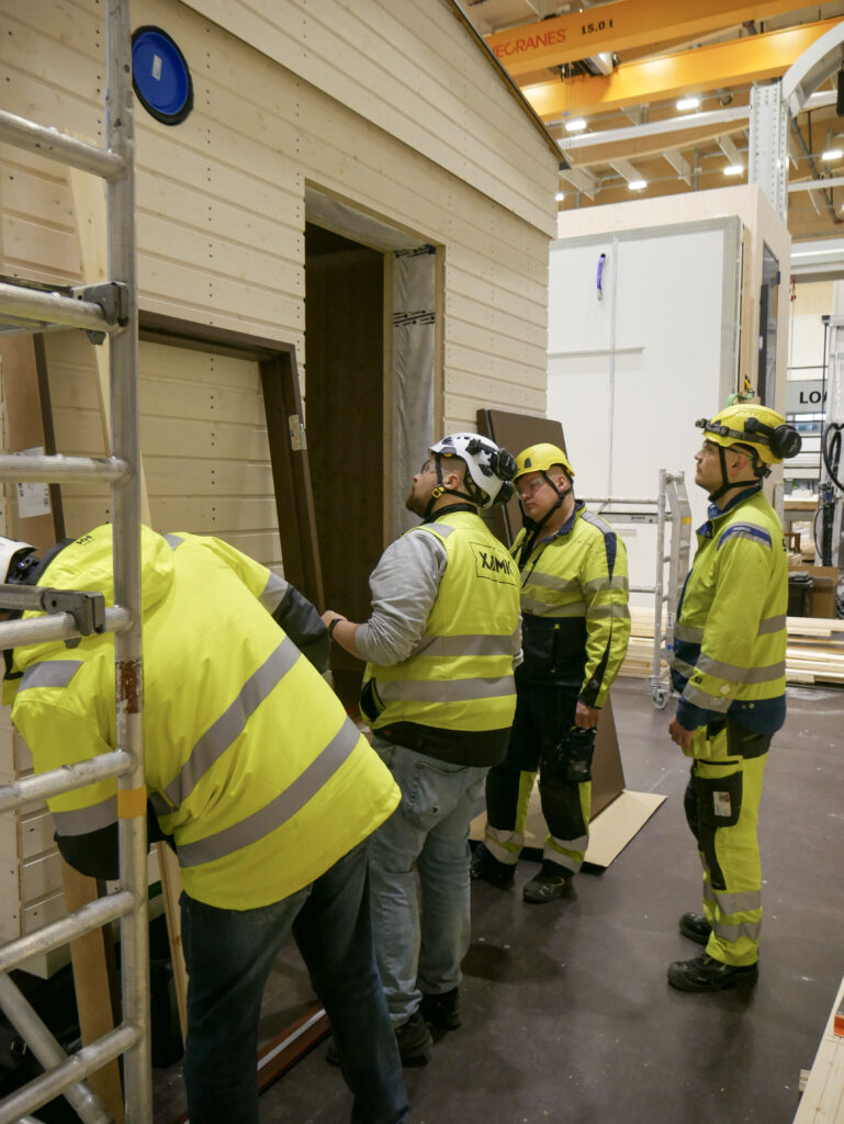 Opettaja ja työnohjaaja tarkastavat rakennetun testitalon työnjälkeä opiskelijoiden kanssa.