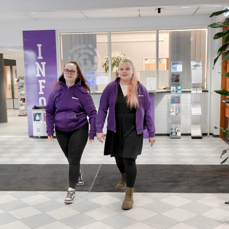 kaksi opiskelijaa Samiedu-huppareissaan kävelee käytävällä kohti kameraa