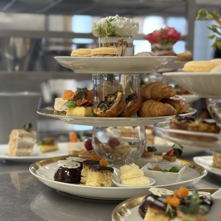 Kuvasa on kolmikerroksinen tarjoiluvati täynnä suolaisia ja makeita herkkuja. Ylimpänä on sokerimassasta valmistettu ruusu.