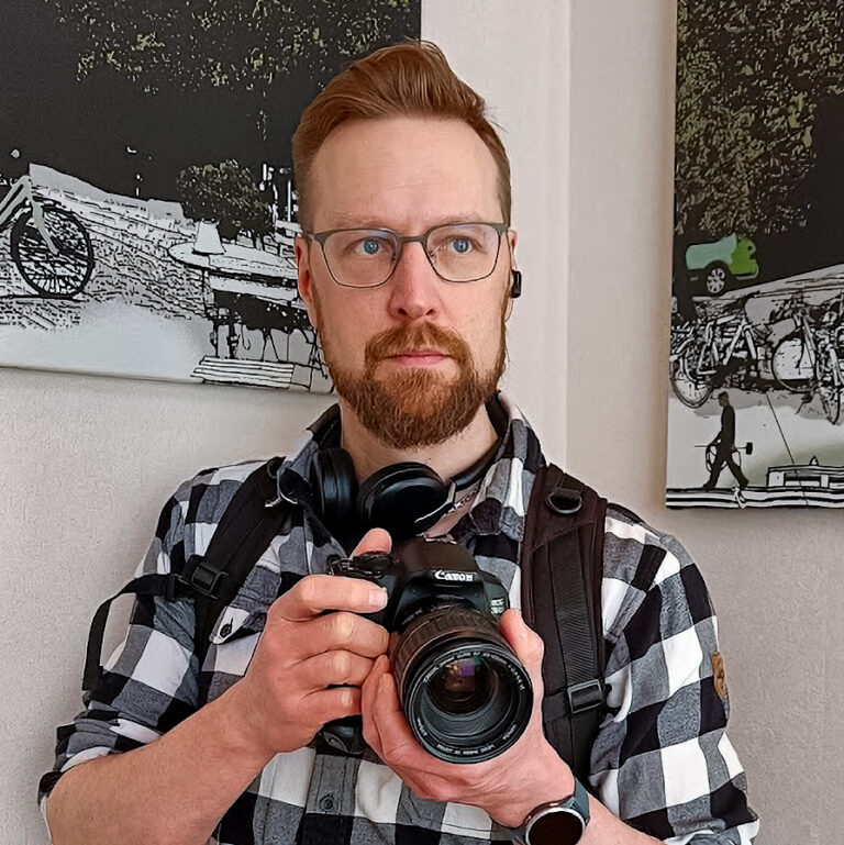 Kuvassa jutun päähenkilö pitää kahdella kädellä järjestelmäkameraa ja katsoo kuvaajaan päin