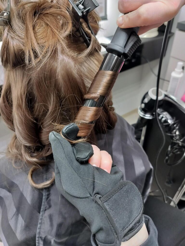 Henkilön ruskeita hiuksia kiharretaan,