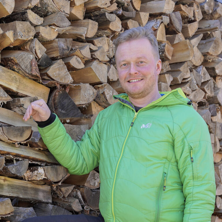 Kuvassa juttuun haastateltu henkilö nojaa kädellään polttopuupinoon.