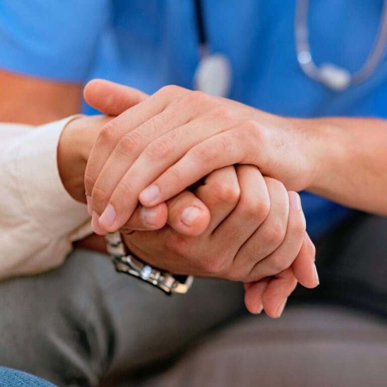 Hoitaja pitää potilasta kädestä. Vain kädet näkyvillä.