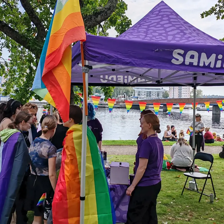 Samiedun teltta ja sateenkaarilippuja pitäviä nuoria Pride-tapahtumassa