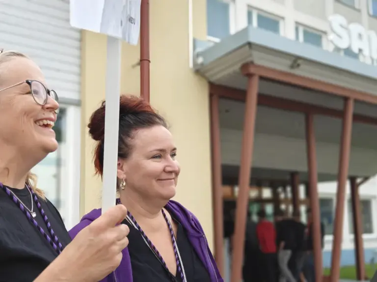 Kaksi opettajaa ottaa hymyillen vastaan uusia opiskelijoita Samiedun pääsisäänkäynnillä. Taustalla näkyy sisälle astuvia opiskelijoita.