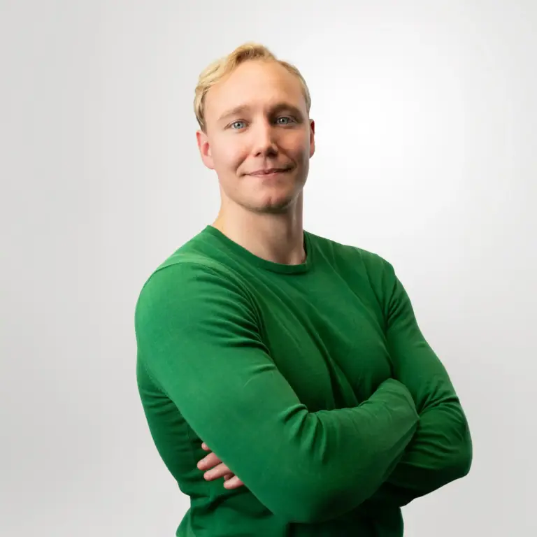 Vihreään paitaan pukeutunut henkilö hymyilee ja katsoo suoraan kameraan.